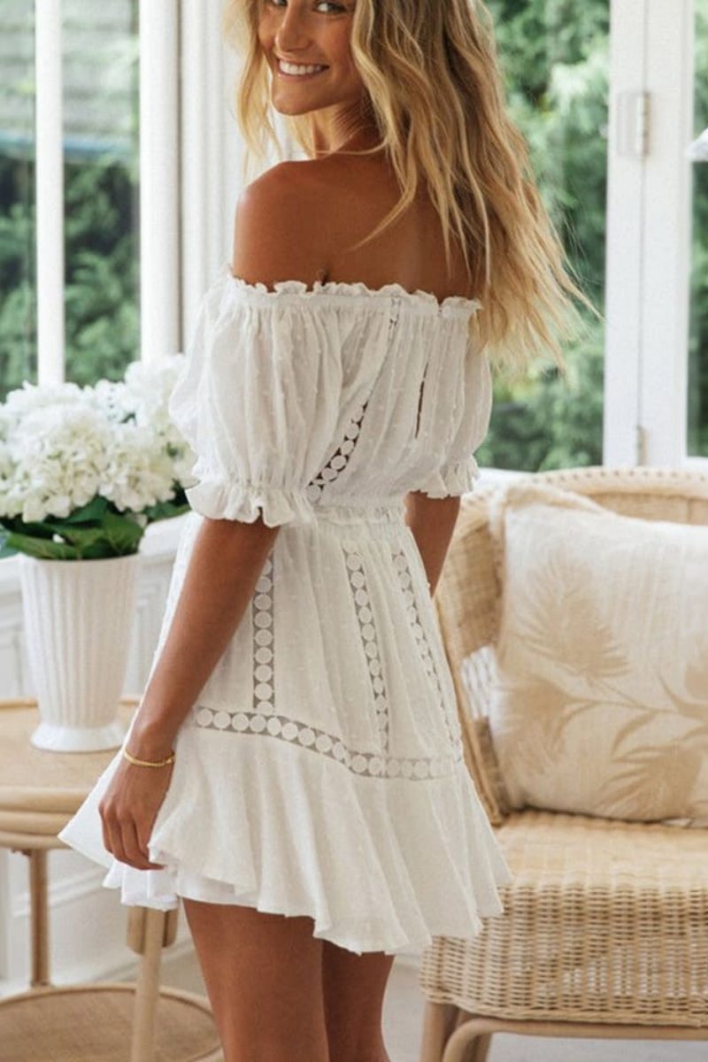 White - Woman wearing a white two-piece set featuring an off-the-shoulder crop top and matching mini skirt, both detailed with crochet lace inserts and ruffled trims.