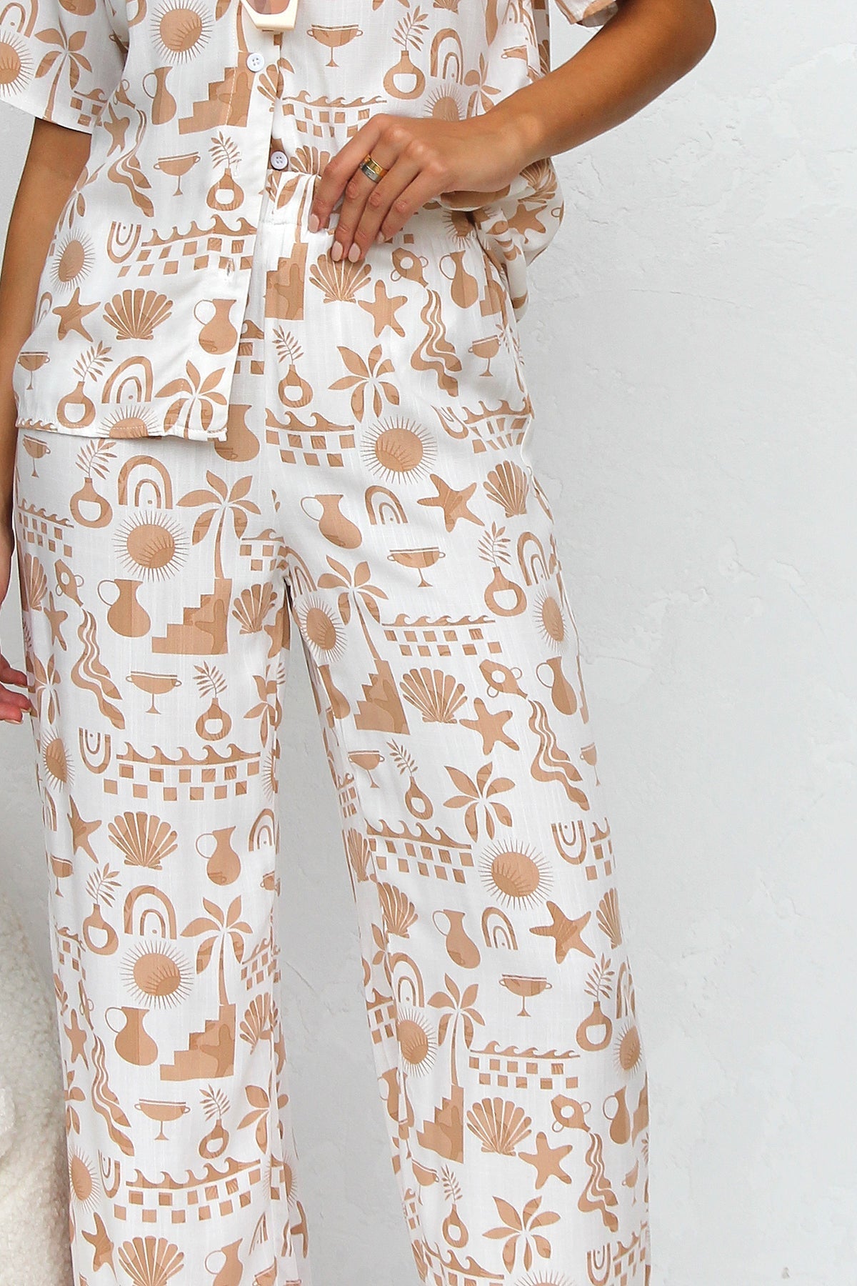 Multicolor - A woman modelling a relaxed-fit, wide-leg trouser and matching short-sleeve shirt co-ord set, featuring a beige coastal vacation print on a white background.