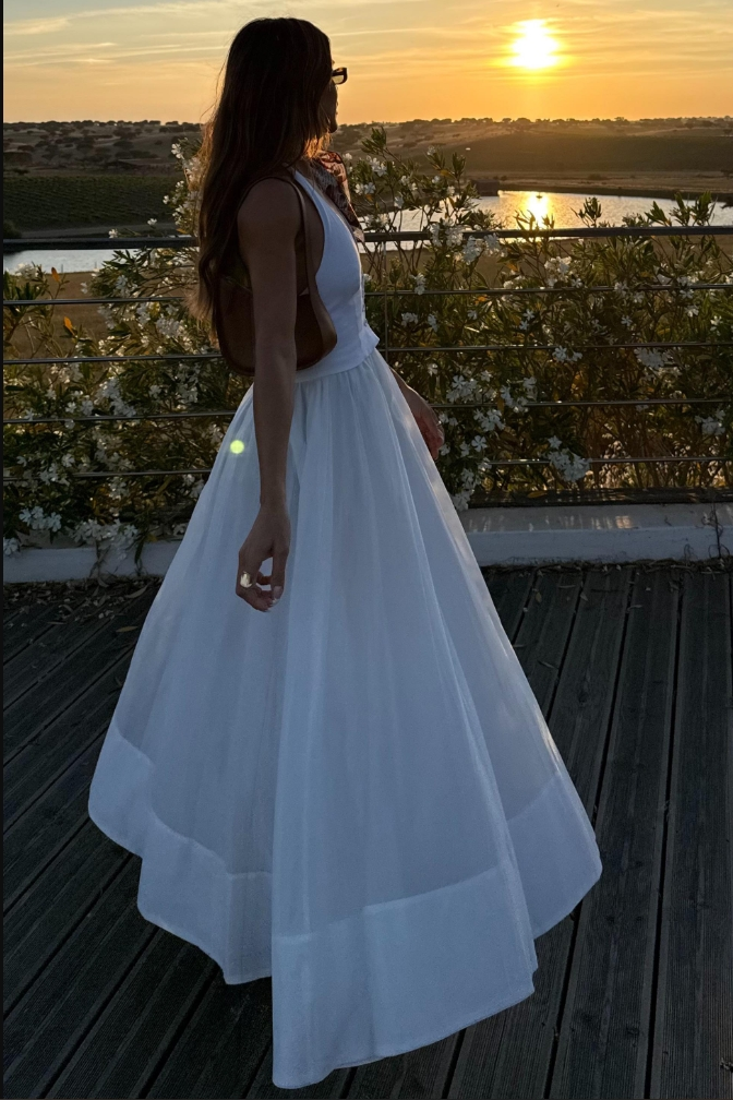 White - A woman models a white sleeveless maxi dress featuring a tailored button-down bodice and a full, gathered skirt with a wide hem band, standing outdoors.