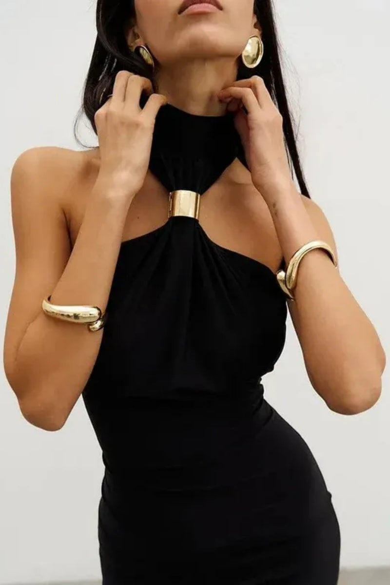 Black - Woman wearing a white form-fitting halterneck maxi dress with a gold ring detail at the neckline, standing indoors.