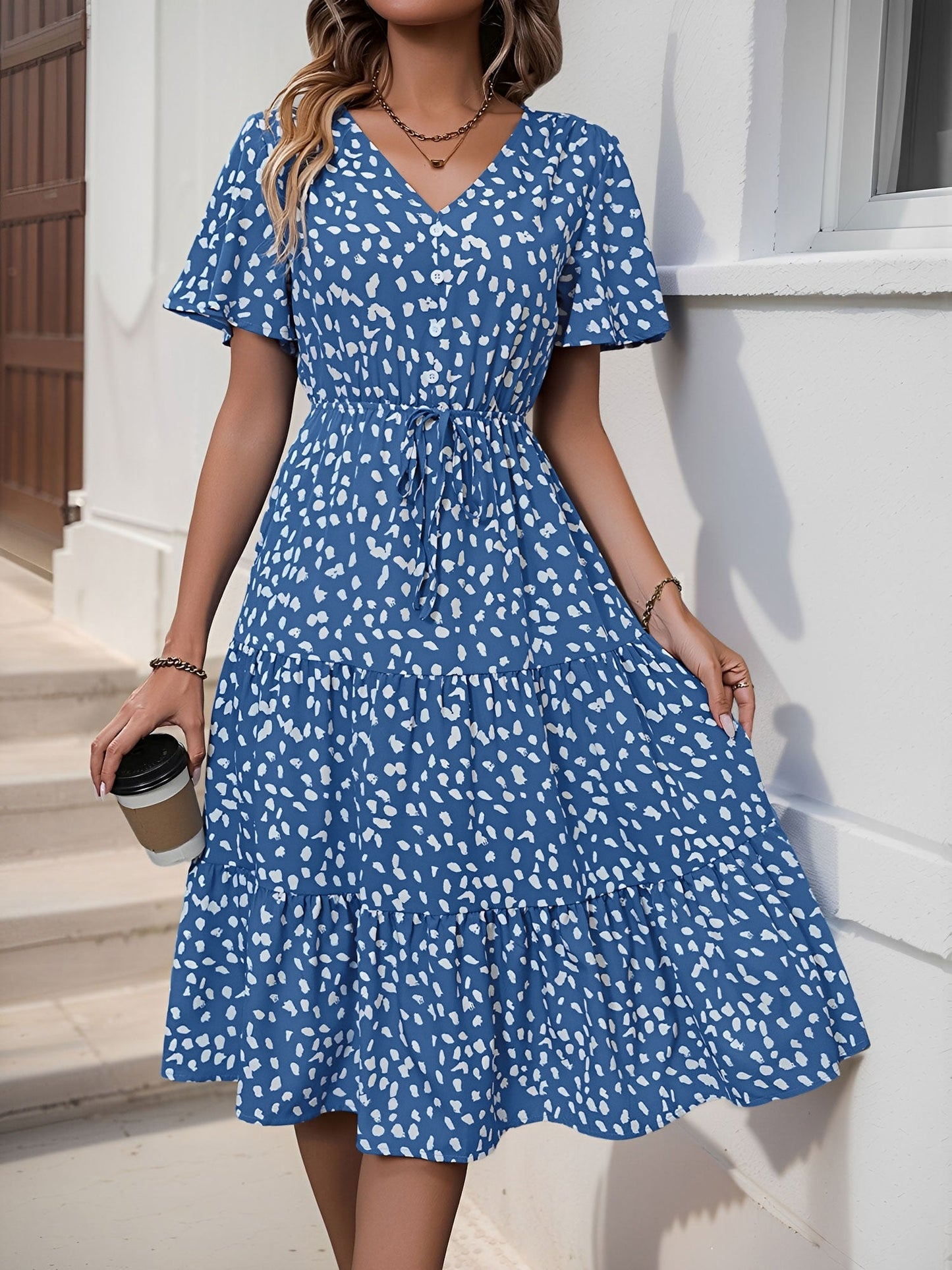 Blue - Woman wearing a spot pattern V-neck tiered midi dress with short sleeves and side pockets, standing in an architectural hallway.