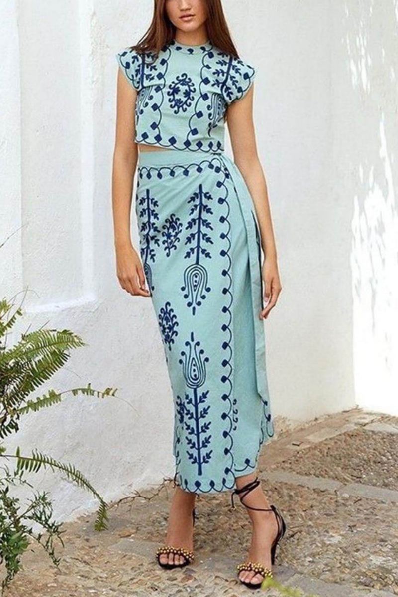 Light green - Women's two-piece set featuring a high-neck sleeveless crop top and a wrap maxi skirt with a side tie, adorned with contrasting folkloric embroidery, worn by a model standing on steps.