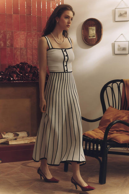 White - Woman wearing an elegant off-white midi knit dress with black contrast binding on the square neckline and straps, a buttoned bodice, and a flared A-line skirt featuring black vertical stripes.