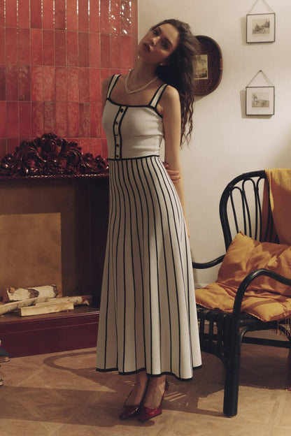 Woman wearing an elegant off-white midi knit dress with black contrast binding on the square neckline and straps, a buttoned bodice, and a flared A-line skirt featuring black vertical stripes.