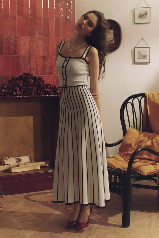 Woman wearing an elegant off-white midi knit dress with black contrast binding on the square neckline and straps, a buttoned bodice, and a flared A-line skirt featuring black vertical stripes.