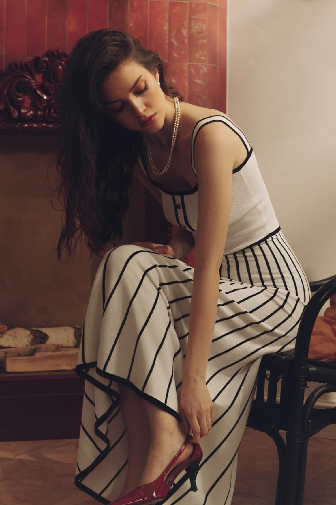 White - Woman wearing an elegant off-white midi knit dress with black contrast binding on the square neckline and straps, a buttoned bodice, and a flared A-line skirt featuring black vertical stripes.
