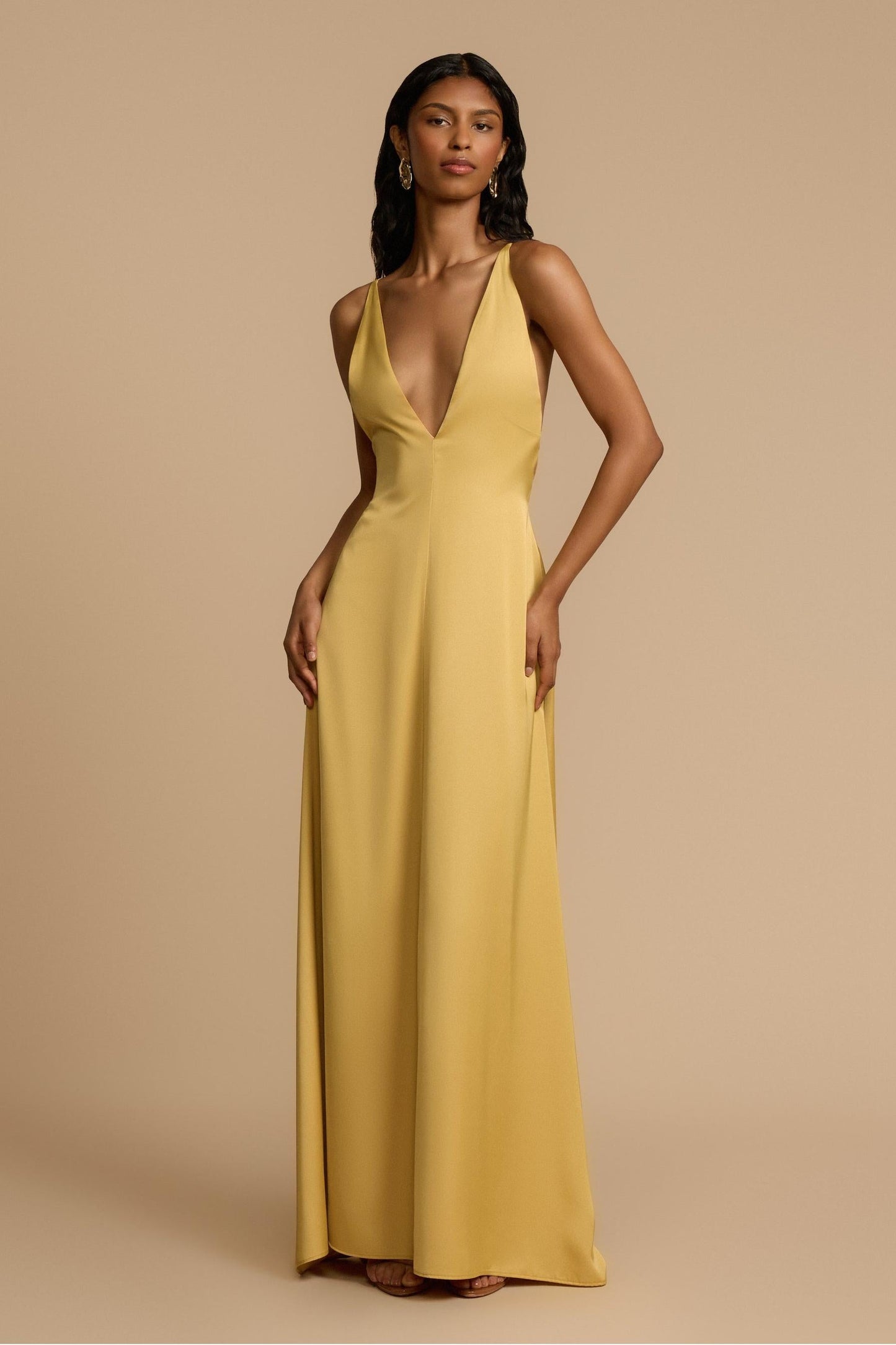 Gold - A woman modelling an elegant, floor-length golden yellow sleeveless maxi dress featuring a deep plunge V-neckline and a smooth, flowing skirt with a subtle satin-like sheen.