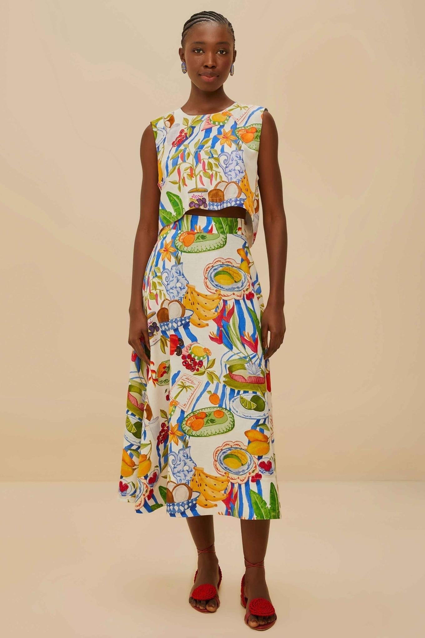 Colorful - Woman wearing a vibrant two-piece co-ord set featuring a sleeveless crop top and high-waisted A-line midi skirt, adorned with a colourful tropical fruit and plate print.