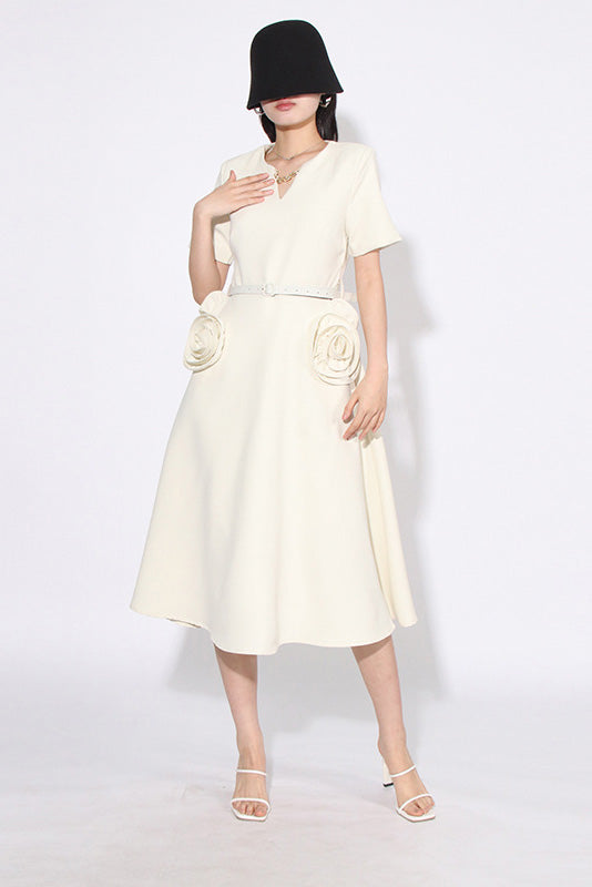 White - A woman wearing a bright red, short-sleeved midi dress featuring a notched V-neckline, a thin waist belt, and two large 3D rosette embellishments on the A-line skirt.