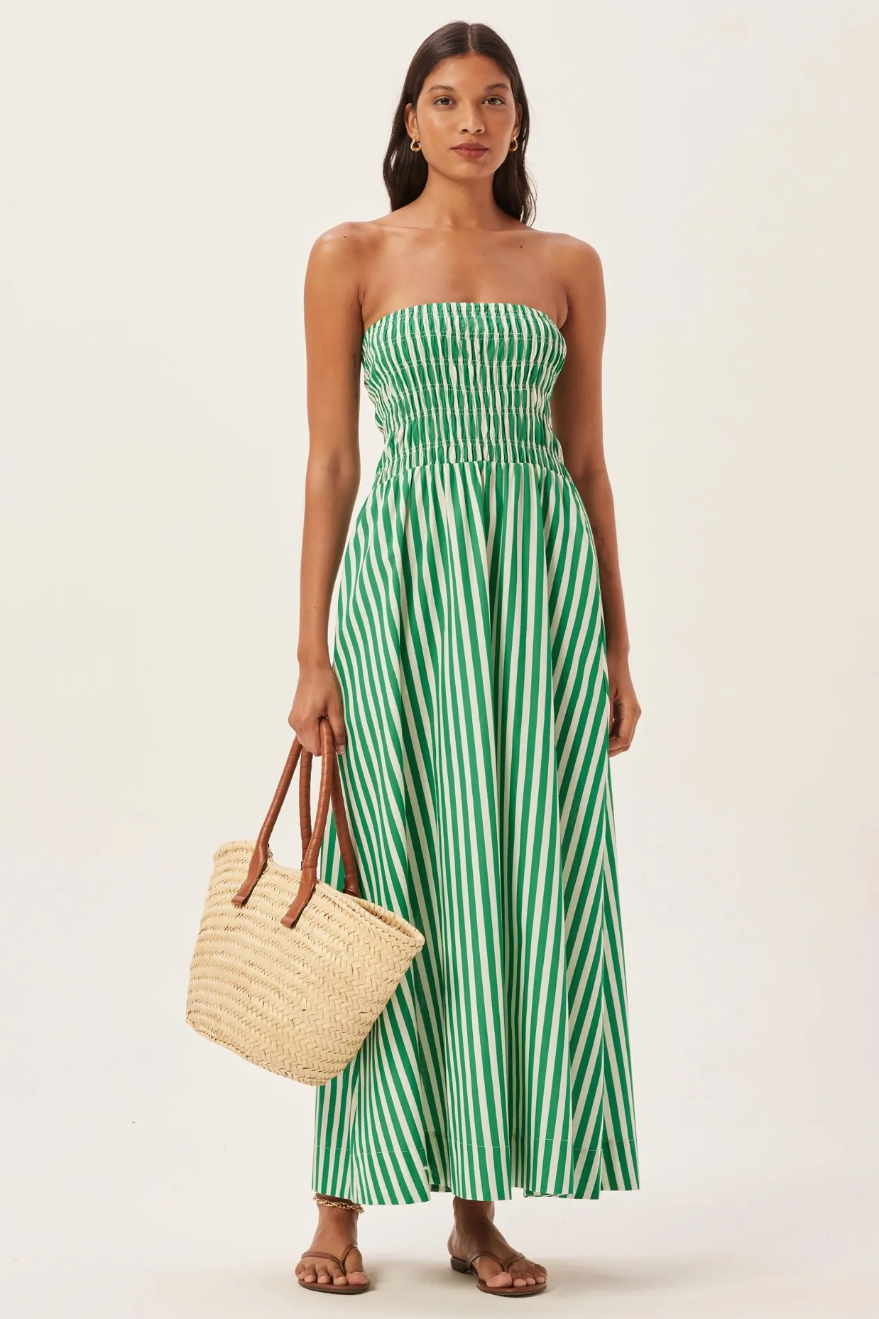 Green - Women's strapless maxi dress featuring a shirred bandeau bodice and bold green and white vertical stripes, styled with a woven straw tote bag.