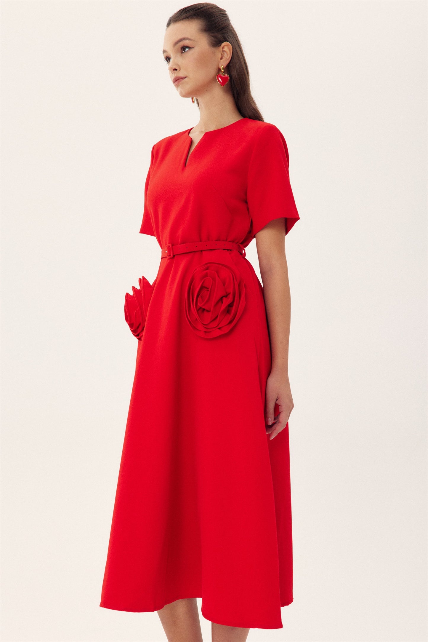 Red - A woman wearing a bright red, short-sleeved midi dress featuring a notched V-neckline, a thin waist belt, and two large 3D rosette embellishments on the A-line skirt.