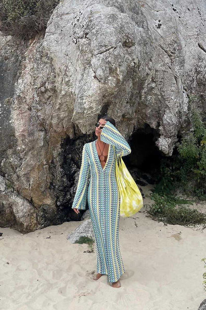 Green - A woman models a textured, open-knit maxi dress featuring a deep V-neck, long bell sleeves, a front slit, and a vertical striped pattern, standing outdoors near pink flowers.