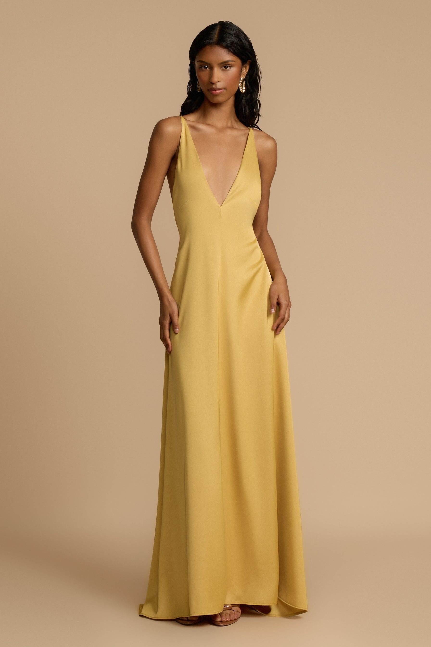 Gold - A woman modelling an elegant, floor-length golden yellow sleeveless maxi dress featuring a deep plunge V-neckline and a smooth, flowing skirt with a subtle satin-like sheen.