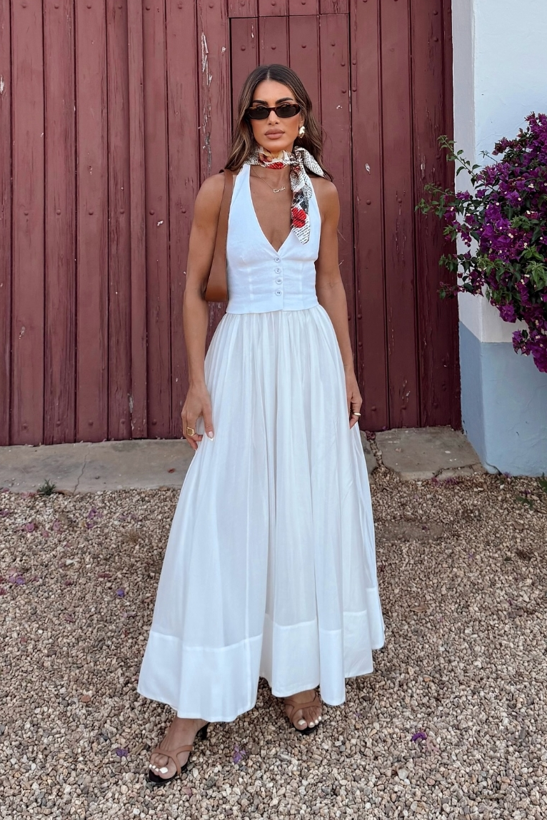 White - A woman models a white sleeveless maxi dress featuring a tailored button-down bodice and a full, gathered skirt with a wide hem band, standing outdoors.