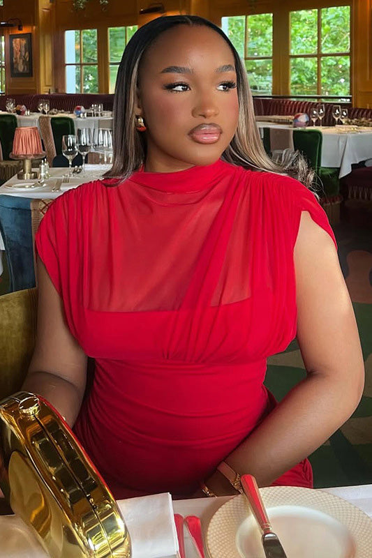 Red - A woman modelling a vibrant red sleeveless maxi dress with a sheer high neckline, ruched bodice, and flowing skirt in an elegant bar setting.