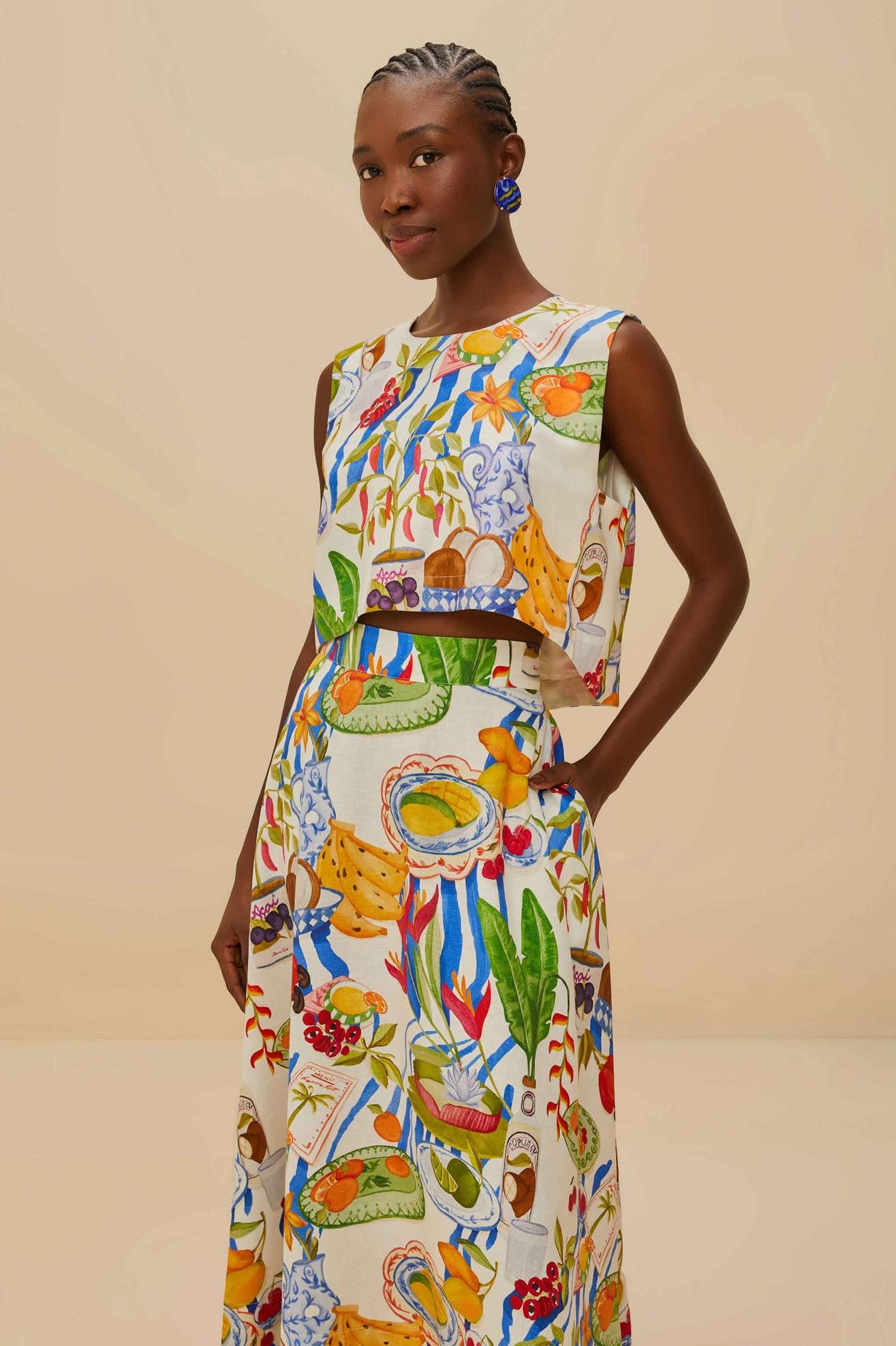 Colorful - Woman wearing a vibrant two-piece co-ord set featuring a sleeveless crop top and high-waisted A-line midi skirt, adorned with a colourful tropical fruit and plate print.