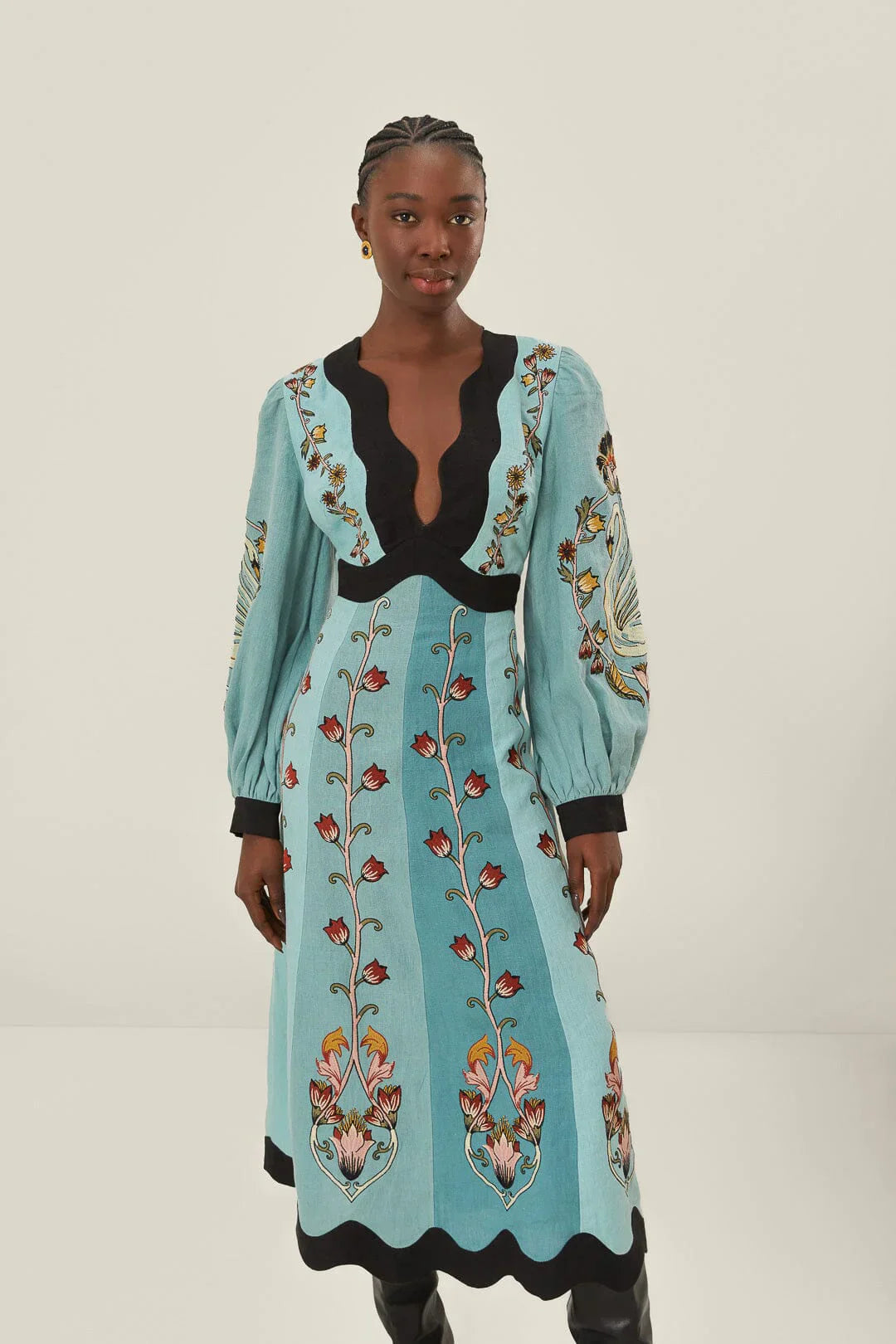 Blue - A woman models a long-sleeve, midi-length dress in shades of blue with a stylized floral print. The dress has a deep V-neckline, voluminous bishop sleeves, and a contrasting black scalloped trim at the neck, cuffs, and hem.