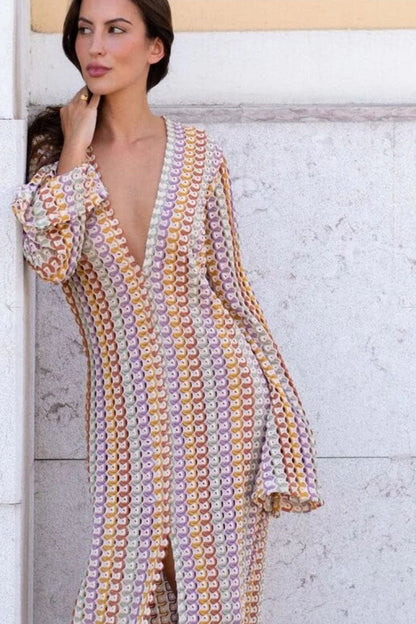 Yellow - A woman models a textured, open-knit maxi dress featuring a deep V-neck, long bell sleeves, a front slit, and a vertical striped pattern, standing outdoors near pink flowers.