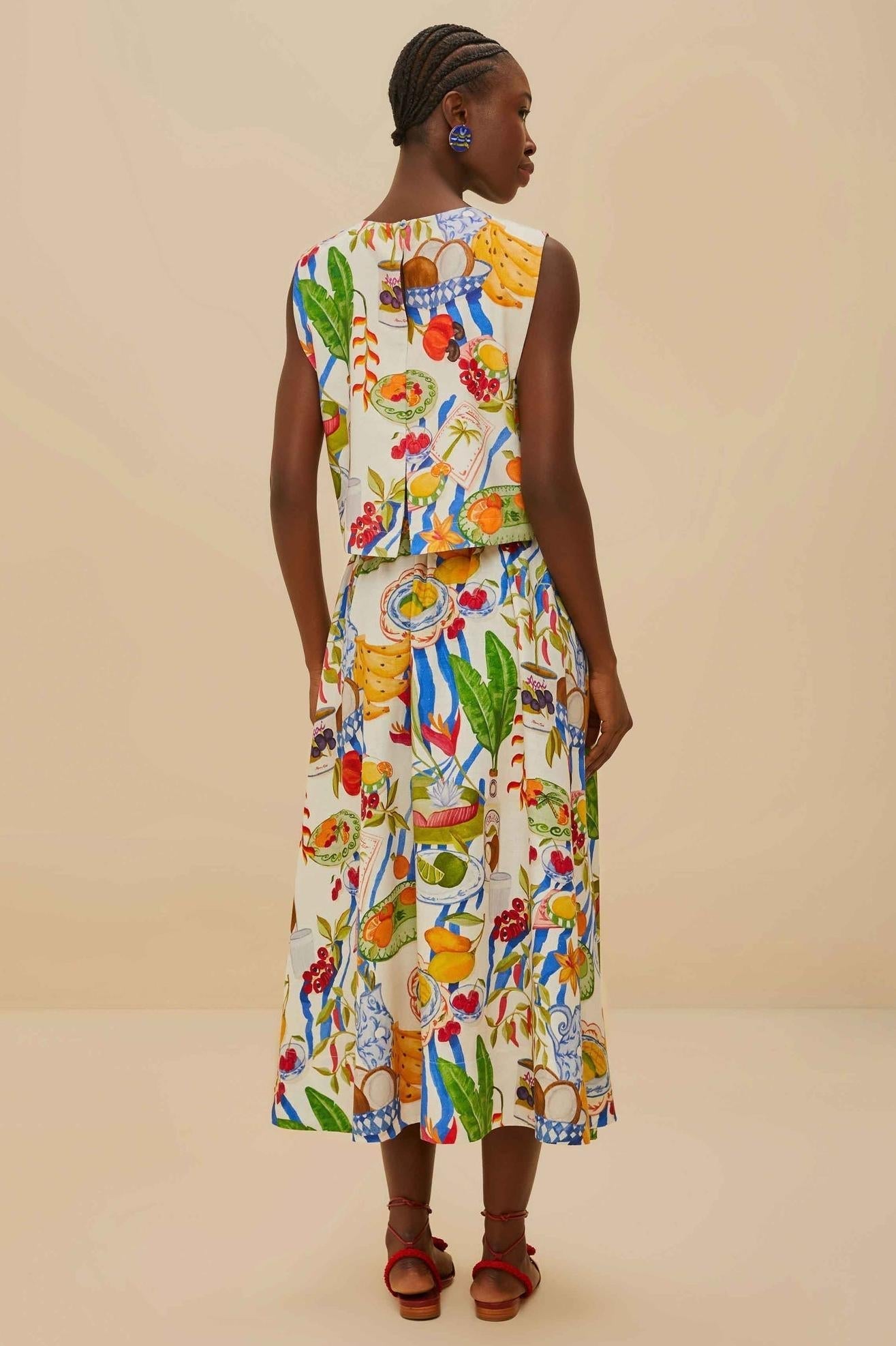 Colorful - Woman wearing a vibrant two-piece co-ord set featuring a sleeveless crop top and high-waisted A-line midi skirt, adorned with a colourful tropical fruit and plate print.