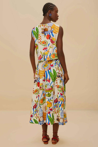Colorful - Woman wearing a vibrant two-piece co-ord set featuring a sleeveless crop top and high-waisted A-line midi skirt, adorned with a colourful tropical fruit and plate print.