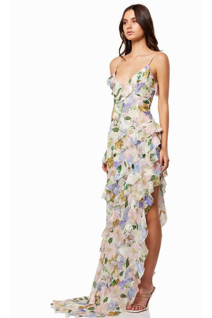 Green - A woman wearing a floor-length, ruffled maxi dress with a pastel floral print on a sheer cream background, featuring spaghetti straps and an asymmetric hem.