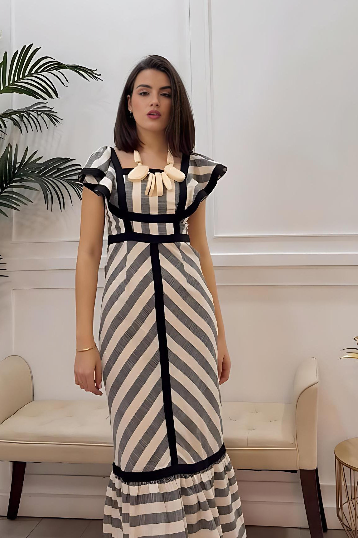 Stripe - A woman wearing a structured maxi dress with a square neckline, ruffled shoulders, and a tiered hem, featuring a bold mixed-direction stripe pattern and contrast black binding.
