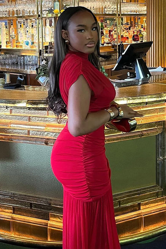 Red - A woman modelling a vibrant red sleeveless maxi dress with a sheer high neckline, ruched bodice, and flowing skirt in an elegant bar setting.