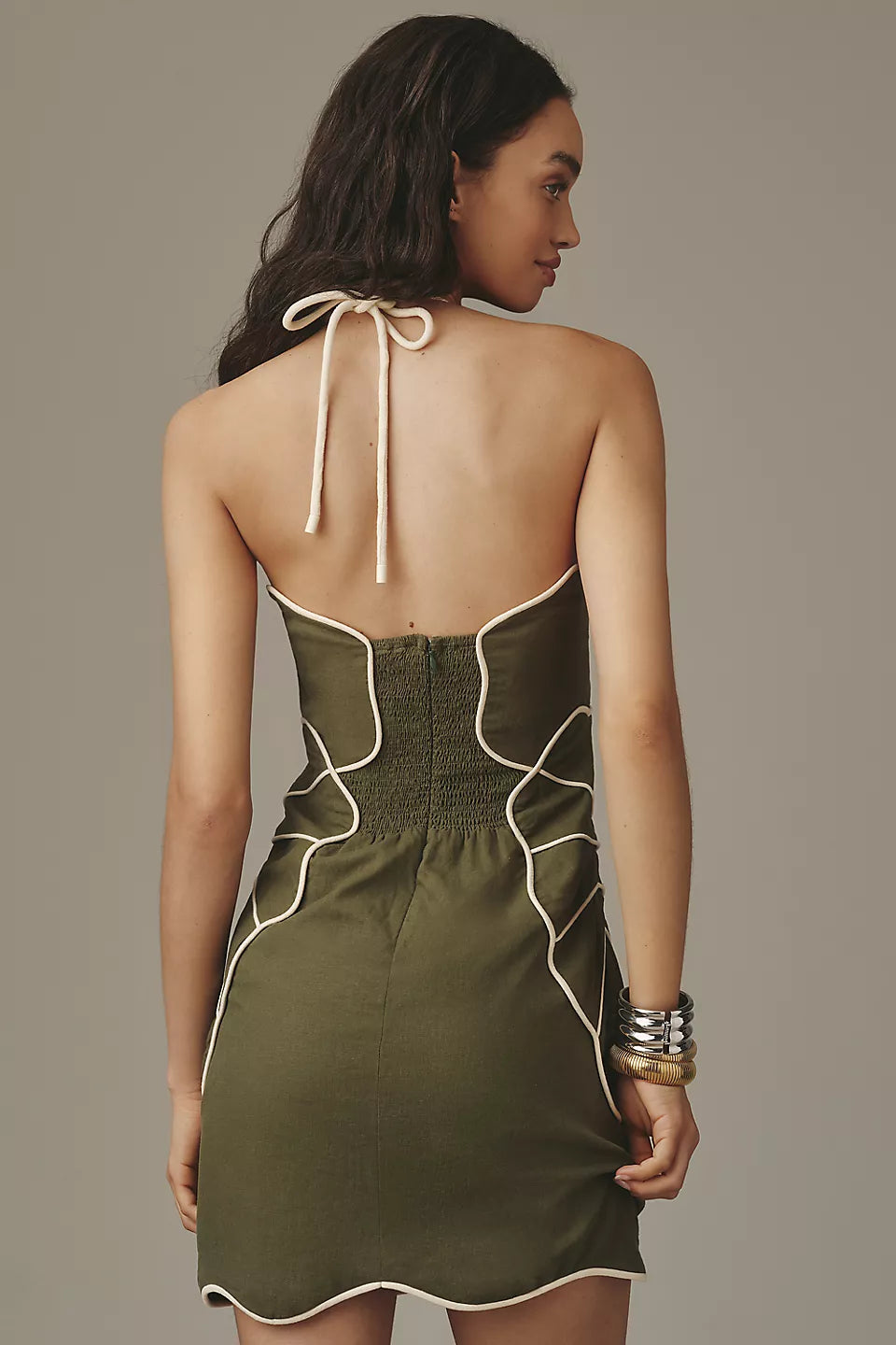 Women's olive green mini dress featuring white contrast piping in a geometric design, with a halterneck tie and structured bodice.