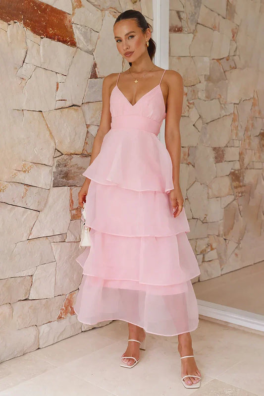 Women's light pink midi dress featuring a V-neckline, spaghetti straps, a wide waistband, and a flowing tiered skirt with a semi-sheer overlay.