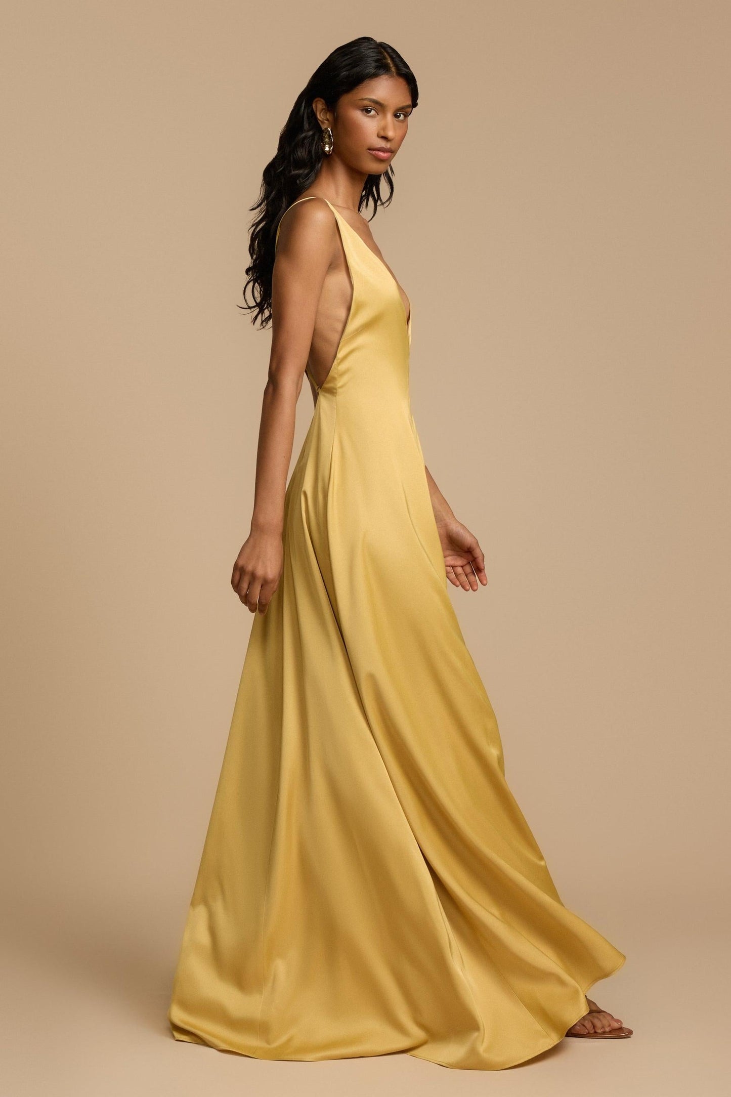 Gold - A woman modelling an elegant, floor-length golden yellow sleeveless maxi dress featuring a deep plunge V-neckline and a smooth, flowing skirt with a subtle satin-like sheen.
