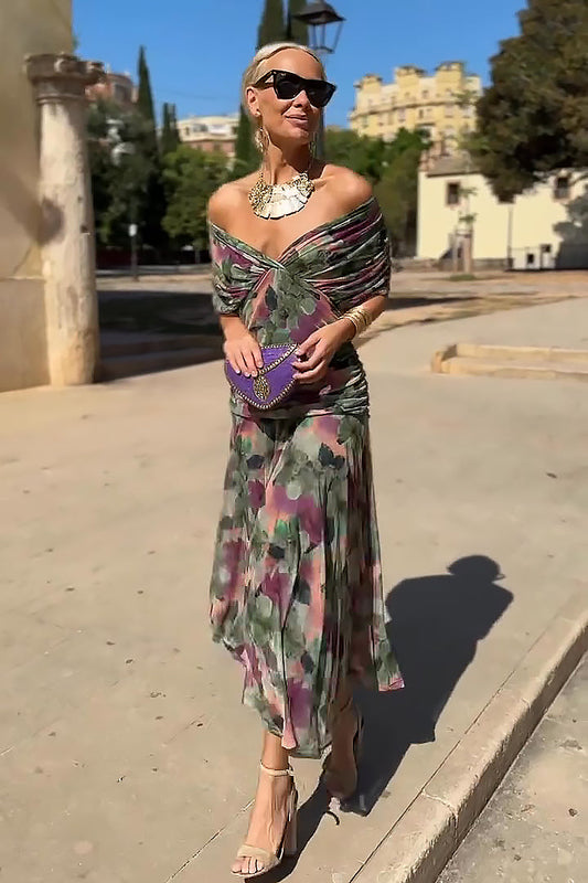 Multi - A woman walking outdoors wearing an elegant off-the-shoulder midi dress featuring a ruched bodice and a muted abstract floral print in shades of green, purple, and pink.