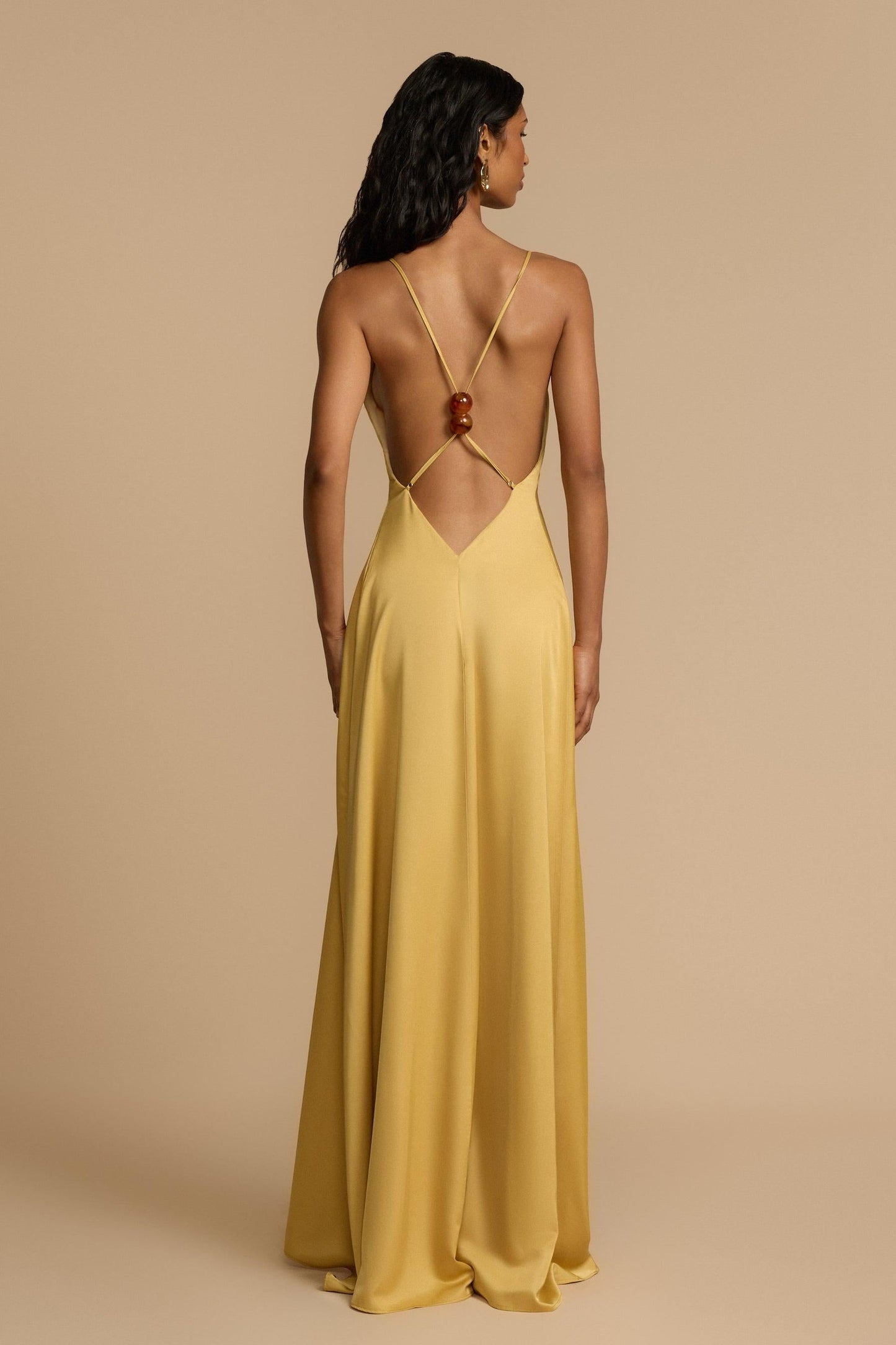 Gold - A woman modelling an elegant, floor-length golden yellow sleeveless maxi dress featuring a deep plunge V-neckline and a smooth, flowing skirt with a subtle satin-like sheen.