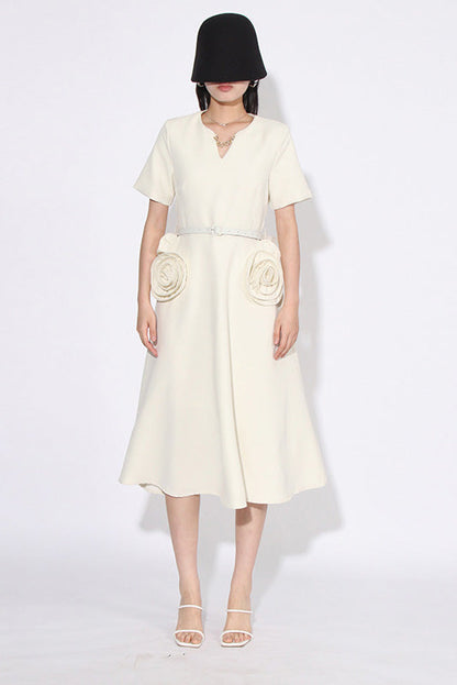 White - A woman wearing a bright red, short-sleeved midi dress featuring a notched V-neckline, a thin waist belt, and two large 3D rosette embellishments on the A-line skirt.