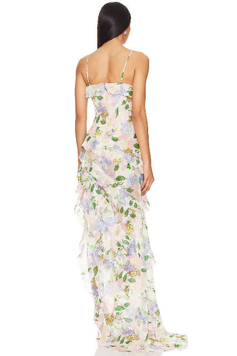 Green - A woman wearing a floor-length, ruffled maxi dress with a pastel floral print on a sheer cream background, featuring spaghetti straps and an asymmetric hem.