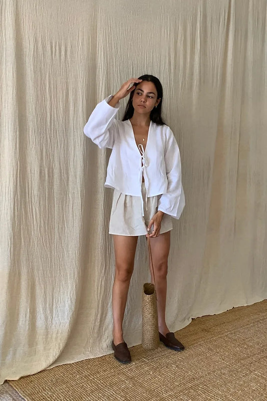White - Women's white long-sleeve holiday blouse featuring a tie-front closure, V-neckline, and a relaxed, breezy fit, styled with neutral tailored shorts.