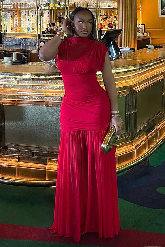 Red - A woman modelling a vibrant red sleeveless maxi dress with a sheer high neckline, ruched bodice, and flowing skirt in an elegant bar setting.