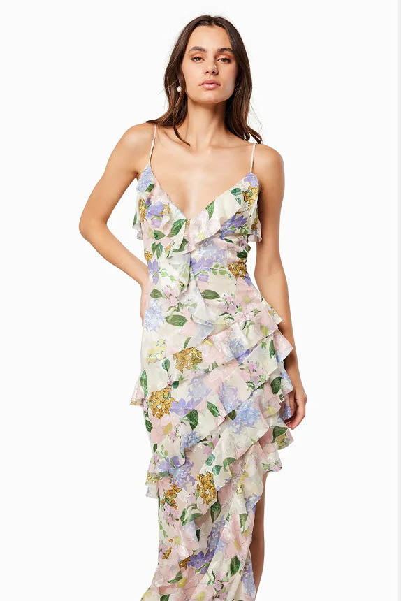 Green - A woman wearing a floor-length, ruffled maxi dress with a pastel floral print on a sheer cream background, featuring spaghetti straps and an asymmetric hem.