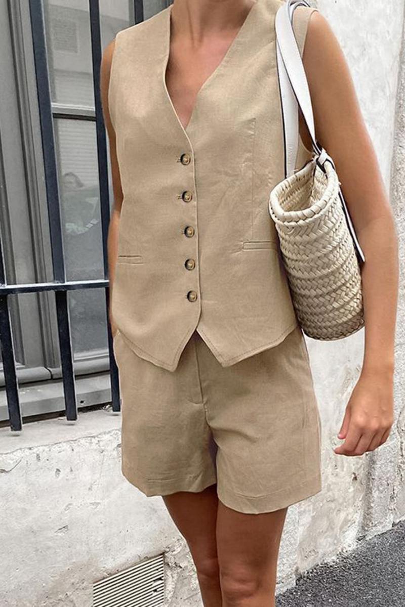 Black - A woman wearing a white, sleeveless, button-front tailored waistcoat top paired with matching high-waisted pleated shorts, standing against a textured white wall.