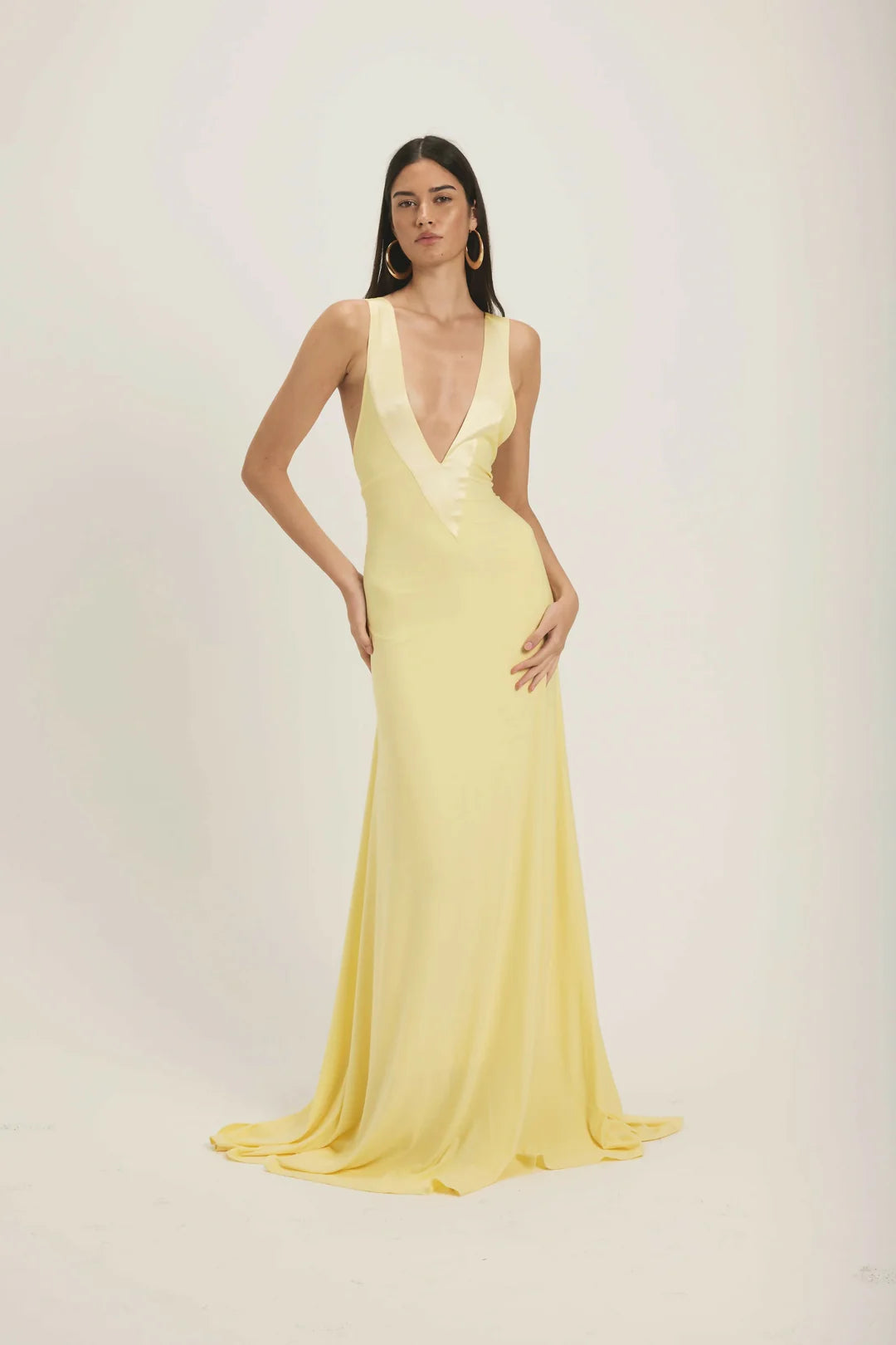 Yellow - A woman modeling a pale yellow, floor-length sleeveless gown featuring a deep plunging V-neckline with a smooth, contrasting trim detail.