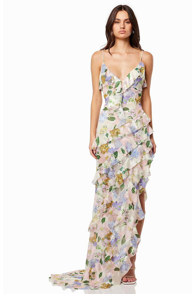 Green - A woman wearing a floor-length, ruffled maxi dress with a pastel floral print on a sheer cream background, featuring spaghetti straps and an asymmetric hem.