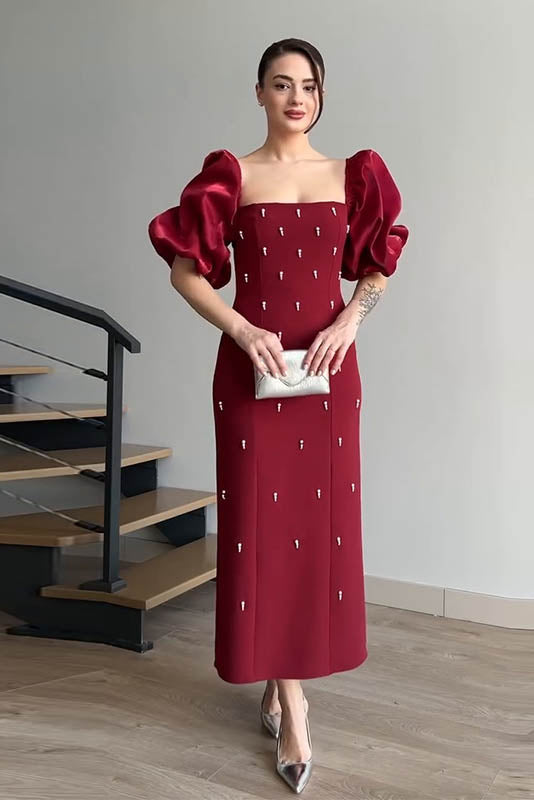 Red - A woman wearing an elegant deep red midi dress featuring large, shiny puff sleeves, a square neckline, and scattered pearl-like embellishments, paired with silver heels and a matching clutch.