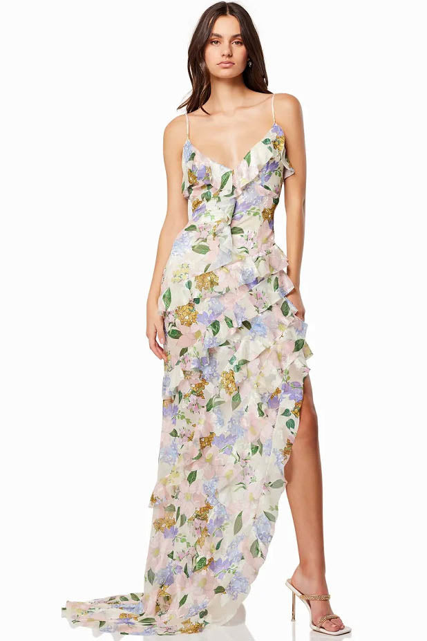 Green - A woman wearing a floor-length, ruffled maxi dress with a pastel floral print on a sheer cream background, featuring spaghetti straps and an asymmetric hem.