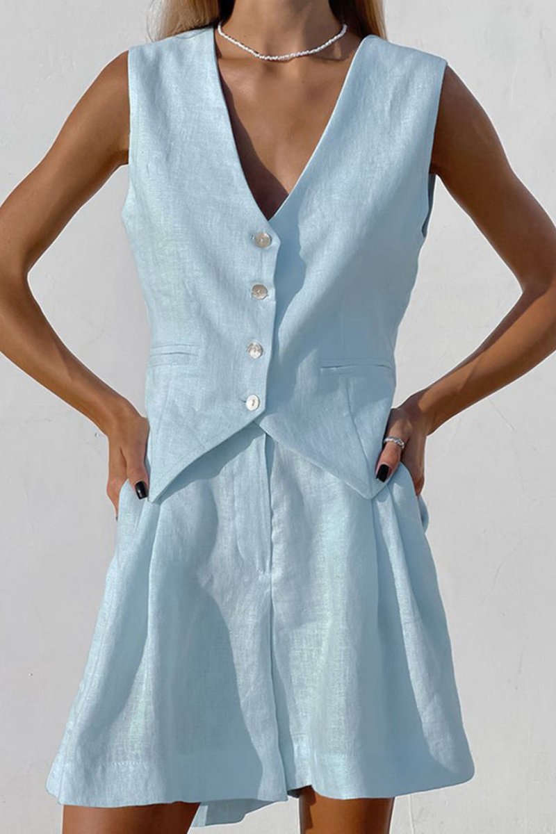 Khaki - A woman wearing a white, sleeveless, button-front tailored waistcoat top paired with matching high-waisted pleated shorts, standing against a textured white wall.