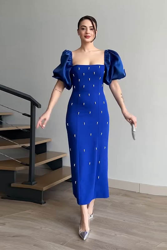 Blue - A woman wearing an elegant deep red midi dress featuring large, shiny puff sleeves, a square neckline, and scattered pearl-like embellishments, paired with silver heels and a matching clutch.