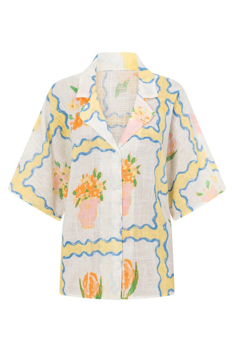 MultiColor - A woman modelling a matching white cropped short-sleeve shirt and mini wrap skirt, decorated with a yellow and blue wavy border pattern and orange floral vase illustrations.