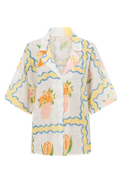 MultiColor - A woman modelling a matching white cropped short-sleeve shirt and mini wrap skirt, decorated with a yellow and blue wavy border pattern and orange floral vase illustrations.