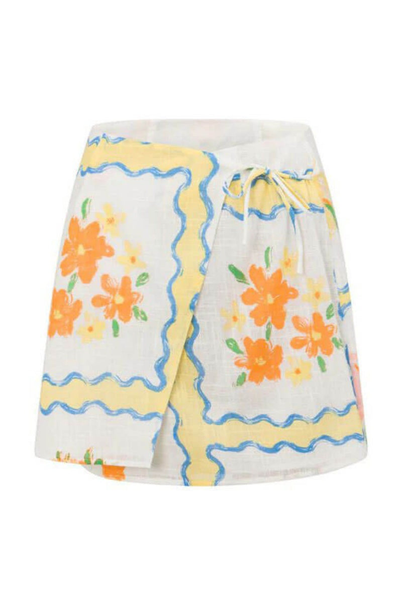 MultiColor - A woman modelling a matching white cropped short-sleeve shirt and mini wrap skirt, decorated with a yellow and blue wavy border pattern and orange floral vase illustrations.
