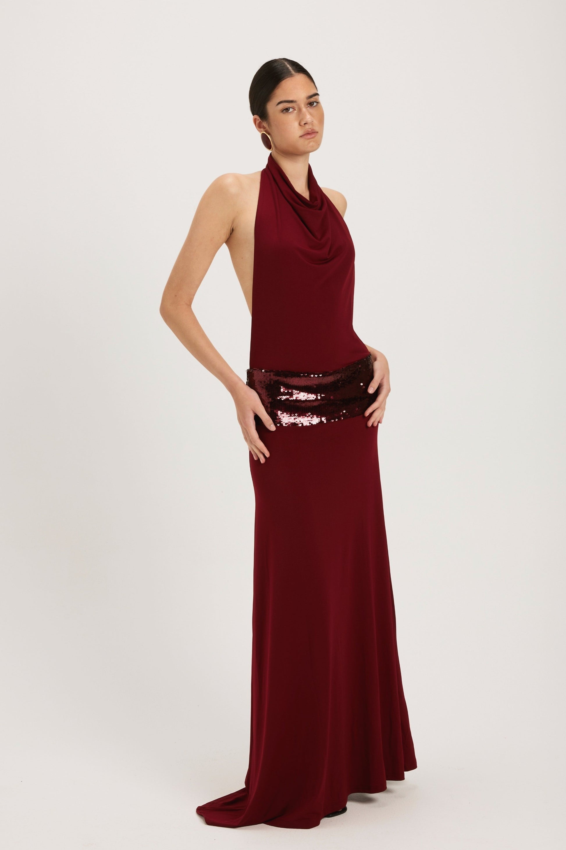 XL - Women's dark red maxi dress featuring a draped cowl halter neckline, an open back, and a wide sequin-embellished band at the waist, falling to a floor-length hem.