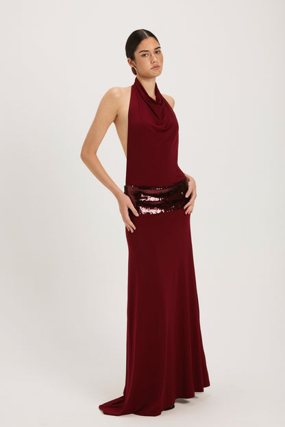 XL - Women's dark red maxi dress featuring a draped cowl halter neckline, an open back, and a wide sequin-embellished band at the waist, falling to a floor-length hem.
