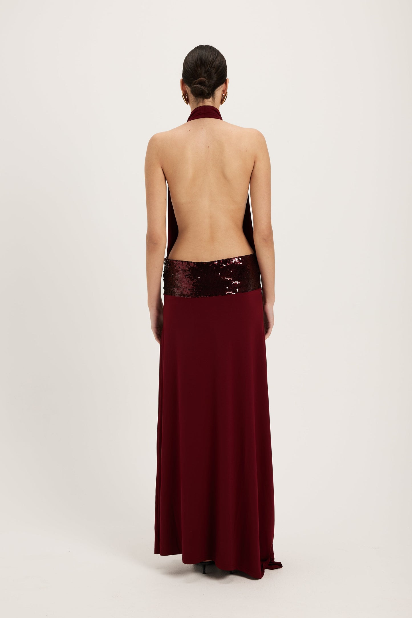 XL - Women's dark red maxi dress featuring a draped cowl halter neckline, an open back, and a wide sequin-embellished band at the waist, falling to a floor-length hem.